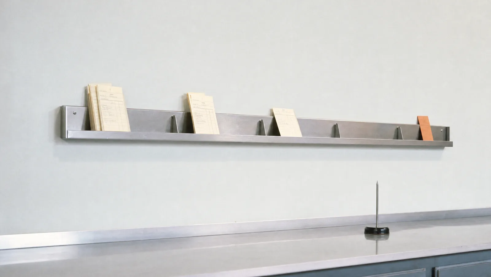 A steel ticket rail split into stages, with cream order slips thinning out towards one orange slip at the end.