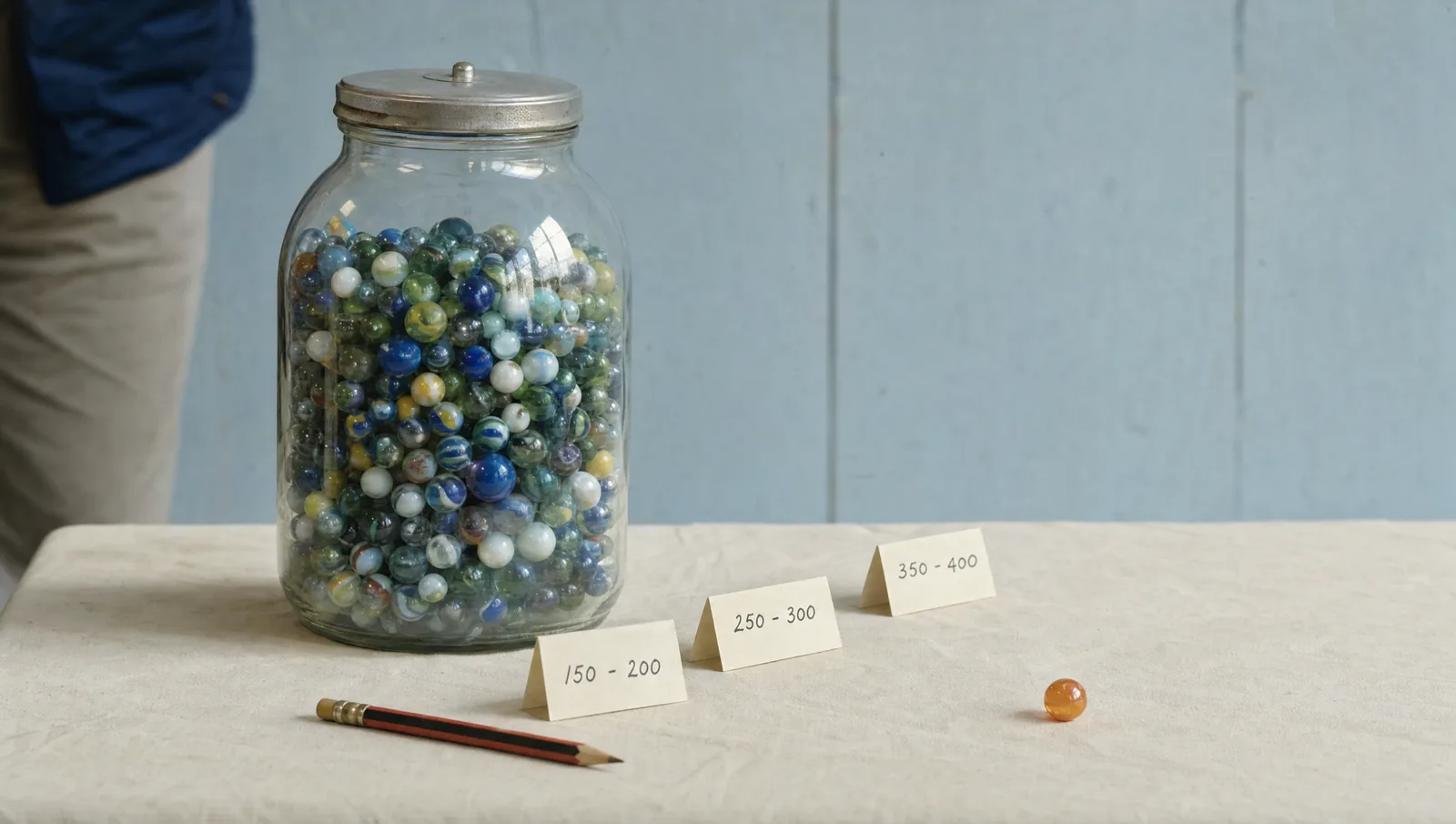 A large jar of marbles on a 1980s fair counter with three folded guess slips in front of it and a single orange marble on the cloth.